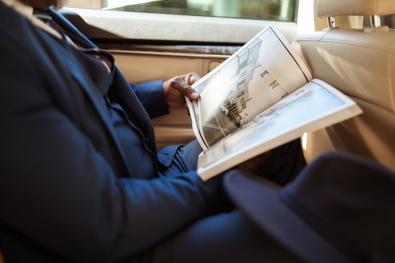 A businessman reads an open book while sitting in the backseat of a car.